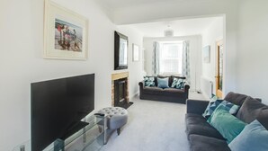 Ein Wohnzimmer mit Flachbildfernseher, Kamin, Sofa und Glastisch.