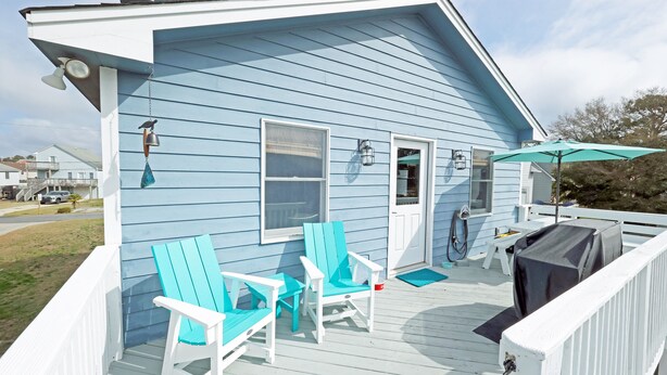 Ein blaues Haus mit Veranda, zwei Stühlen, einem Tisch und einem Grill.