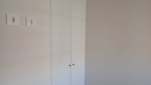 A room with a large wardrobe, a light-colored floor, and two wall-mounted electrical outlets.