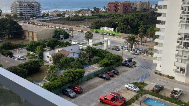 A residential area with a view of the sea, a swimming pool, and several parked cars.