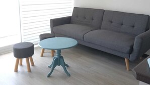 A modern living room with a grey sofa, a round blue table, and two black ottomans.