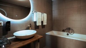 Un baño moderno con un espejo redondo, un tocador de madera, un lavamanos blanco y una bañera.