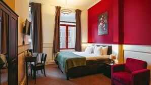 Una habitación de hotel con cama, escritorio, silla y sillón rojo.