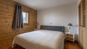 Une chambre avec un mur en bois, un grand lit, deux tables de chevet et une fenêtre avec des rideaux.