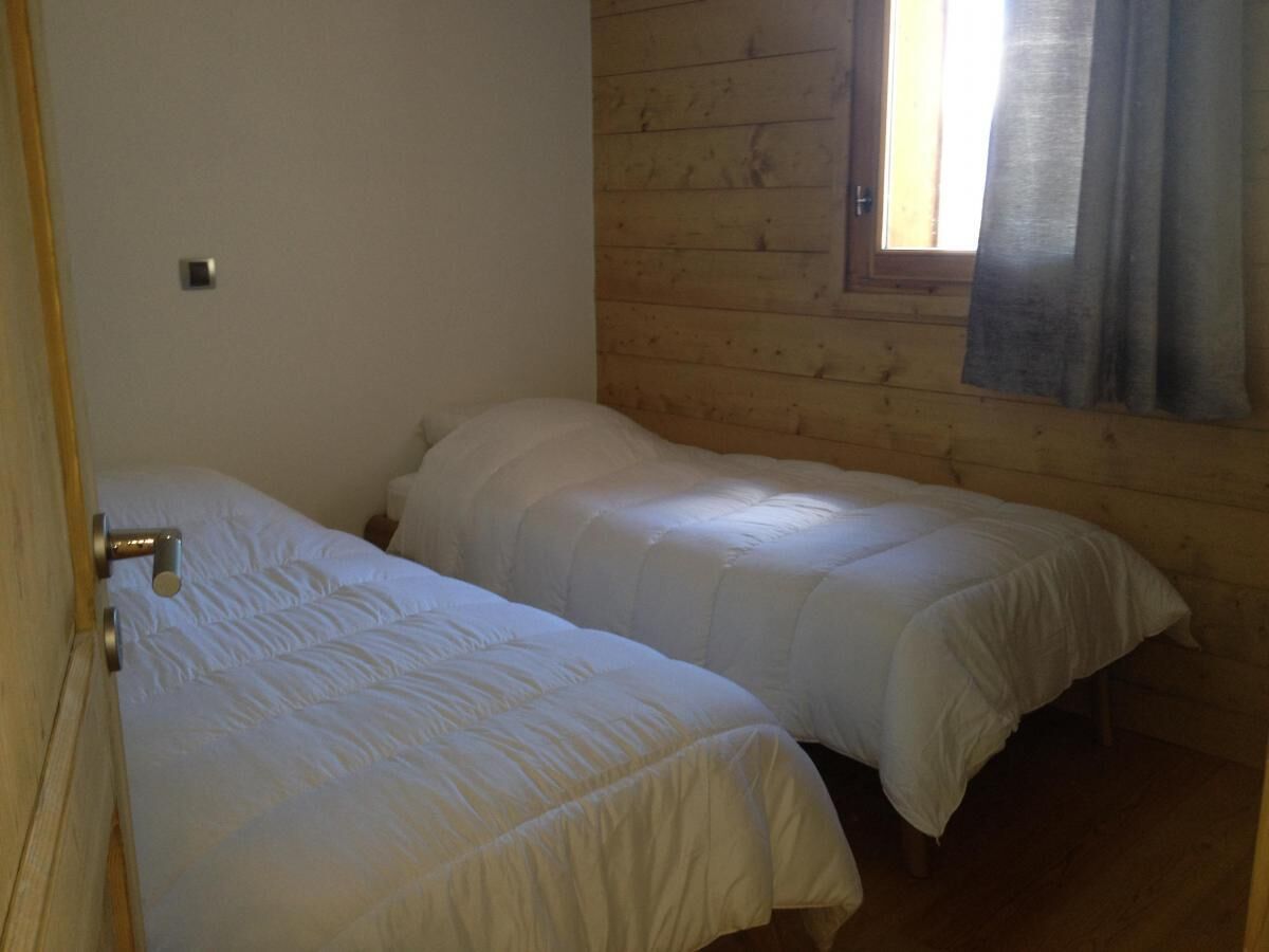 A room with two single beds, wooden walls, a window with curtains, and a door with a handle.