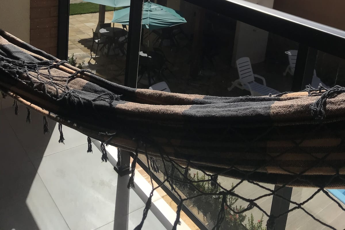 A balcony with a hammock, a glass railing, and a view of an outdoor patio with chairs and a table.
