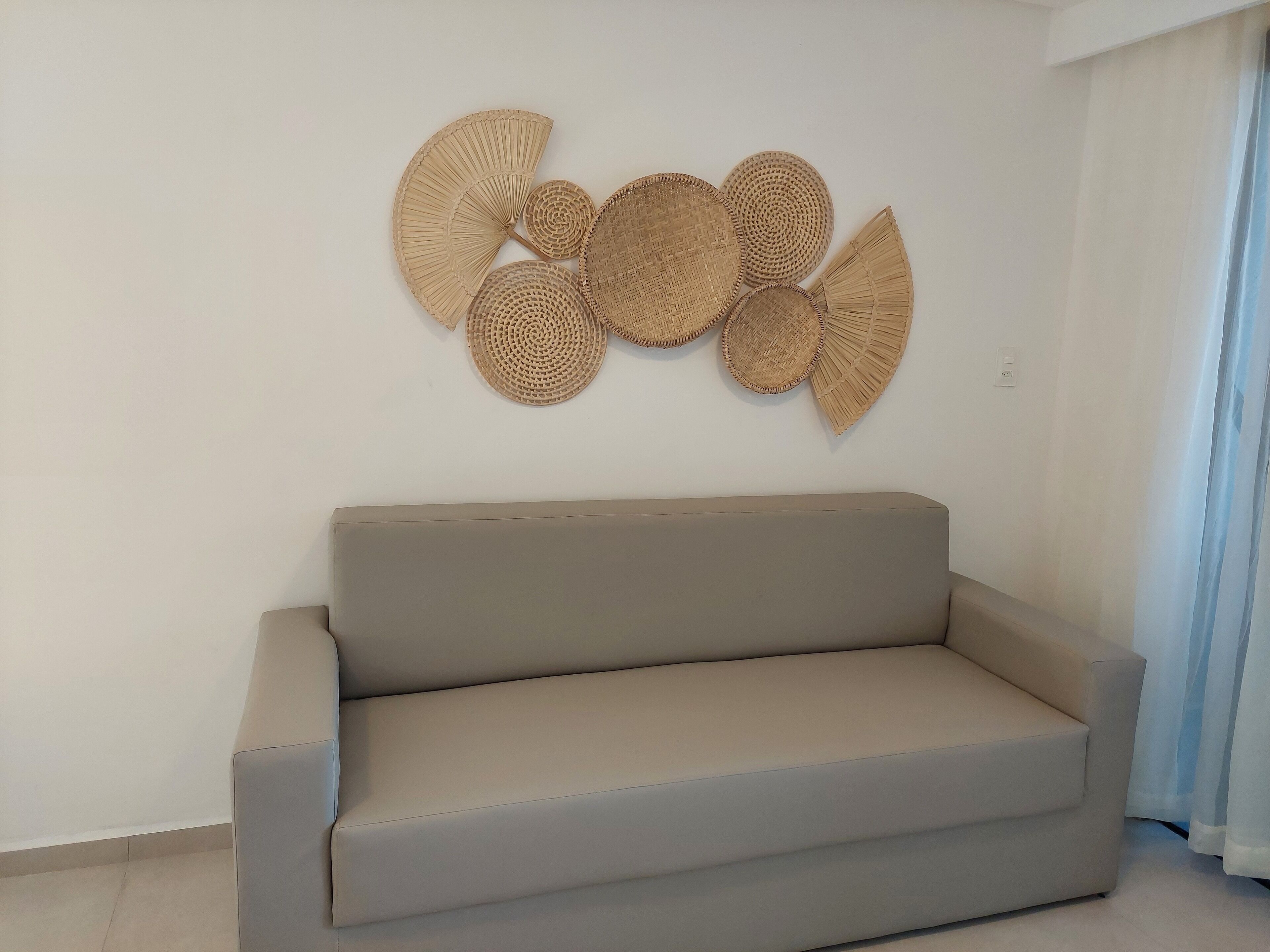 A beige sofa in a room with a white wall and a window with curtains.