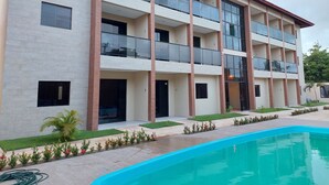Un hotel de varios pisos con balcones, piscina y jardín ajardinado.