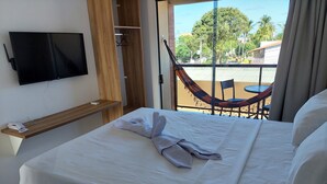 Habitación de hotel con cama, televisor montado en la pared, estante de madera con un teléfono y vista a una hamaca afuera.