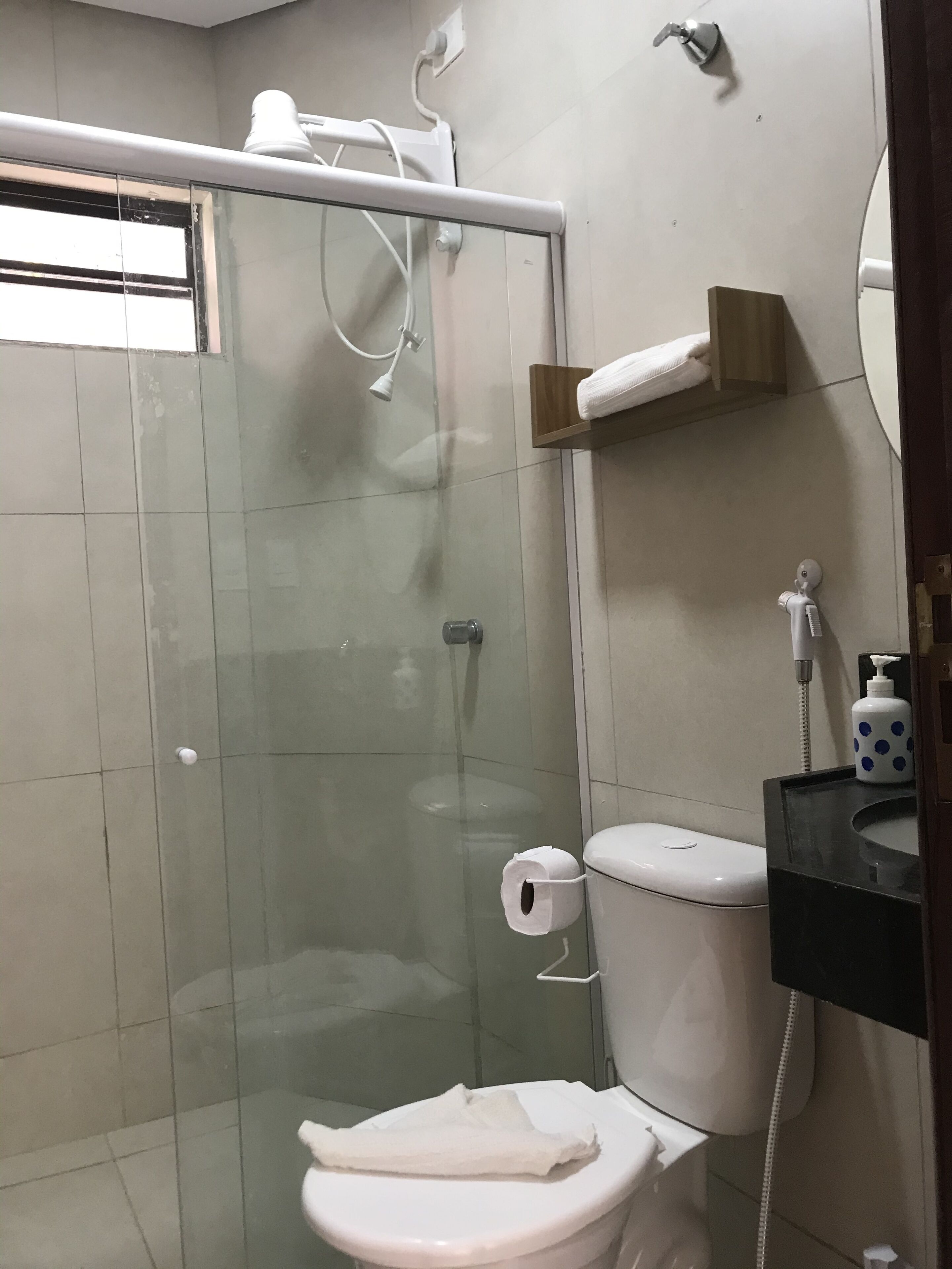 A bathroom with a glass-enclosed shower, a toilet, a sink with a soap dispenser, and a towel rack.