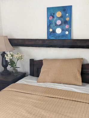 Un dormitorio con una cama, una mesita de noche con una lámpara y flores, y un cuadro en la pared.