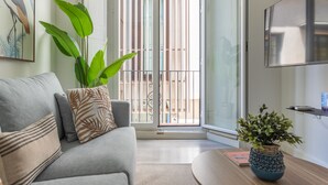 Un salon moderne avec un canapé gris, une grande plante verte et un vase bleu posé sur une table en bois.