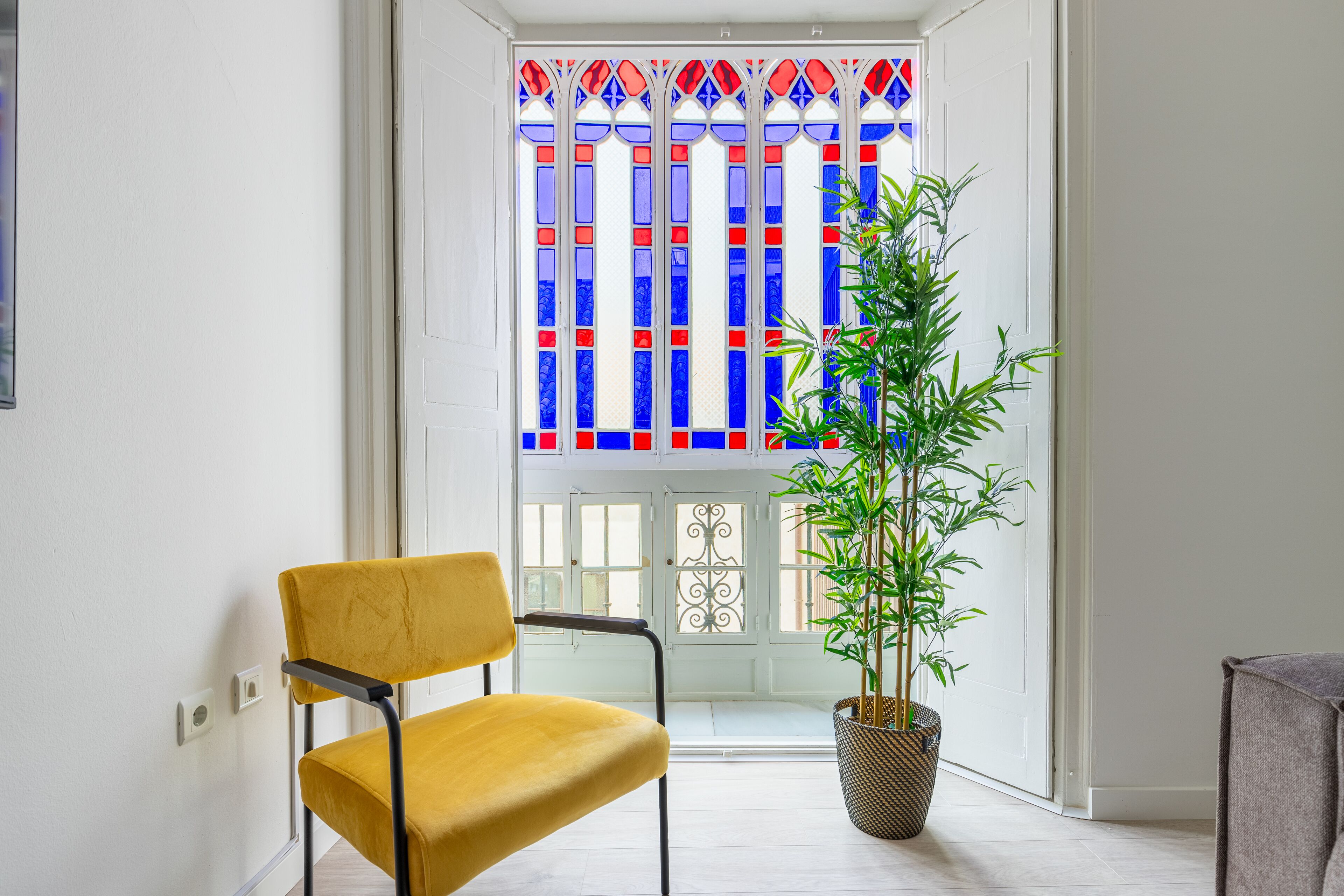 A room with a yellow chair, a potted plant, and a stained glass window.