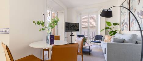 A modern living room with a white sofa, a grey couch, a round dining table with chairs, a TV, and a large plant.