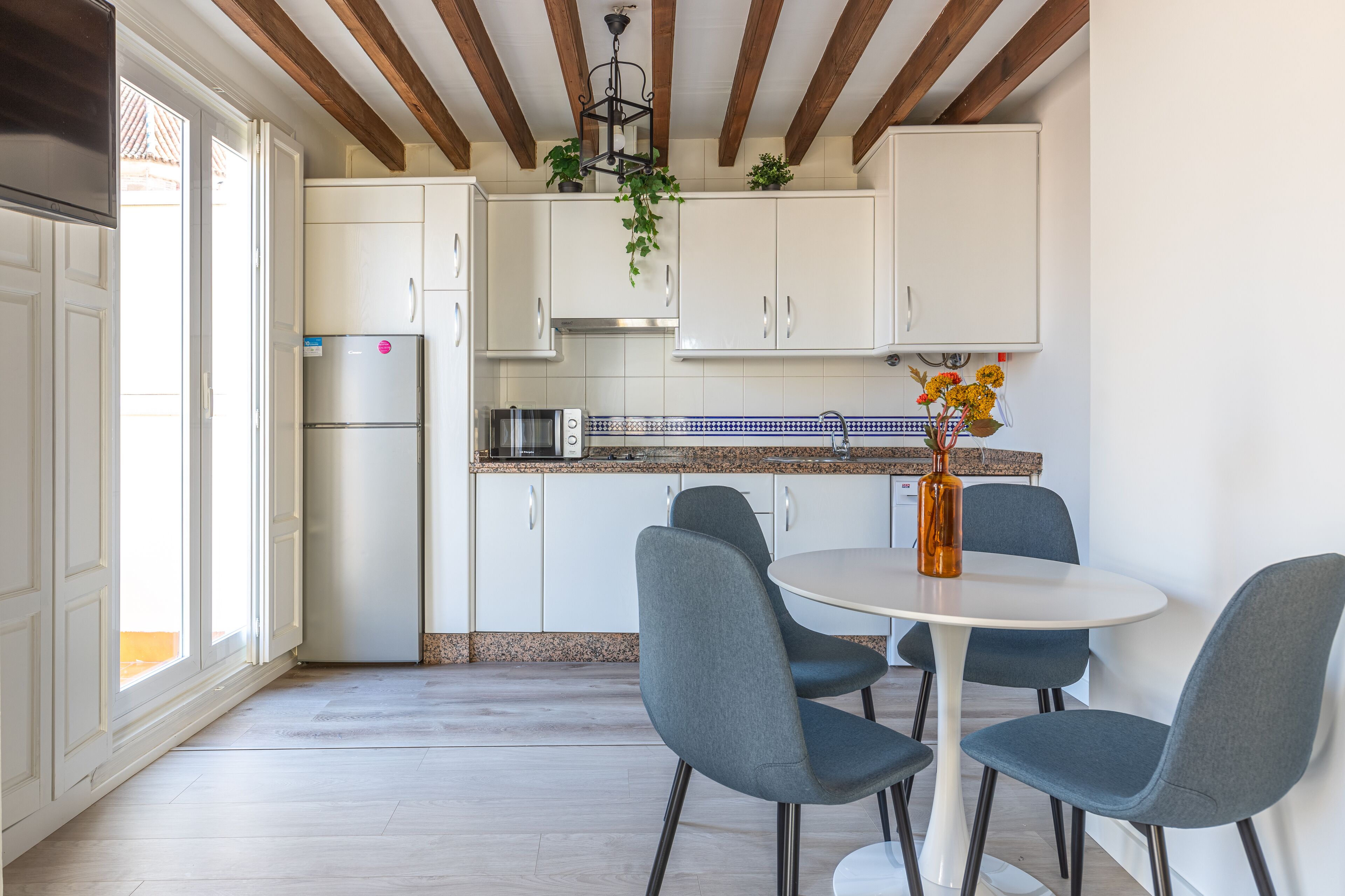 A modern kitchen with white cabinets, a stainless steel refrigerator, a microwave, and a dining area with a round table and four chairs.