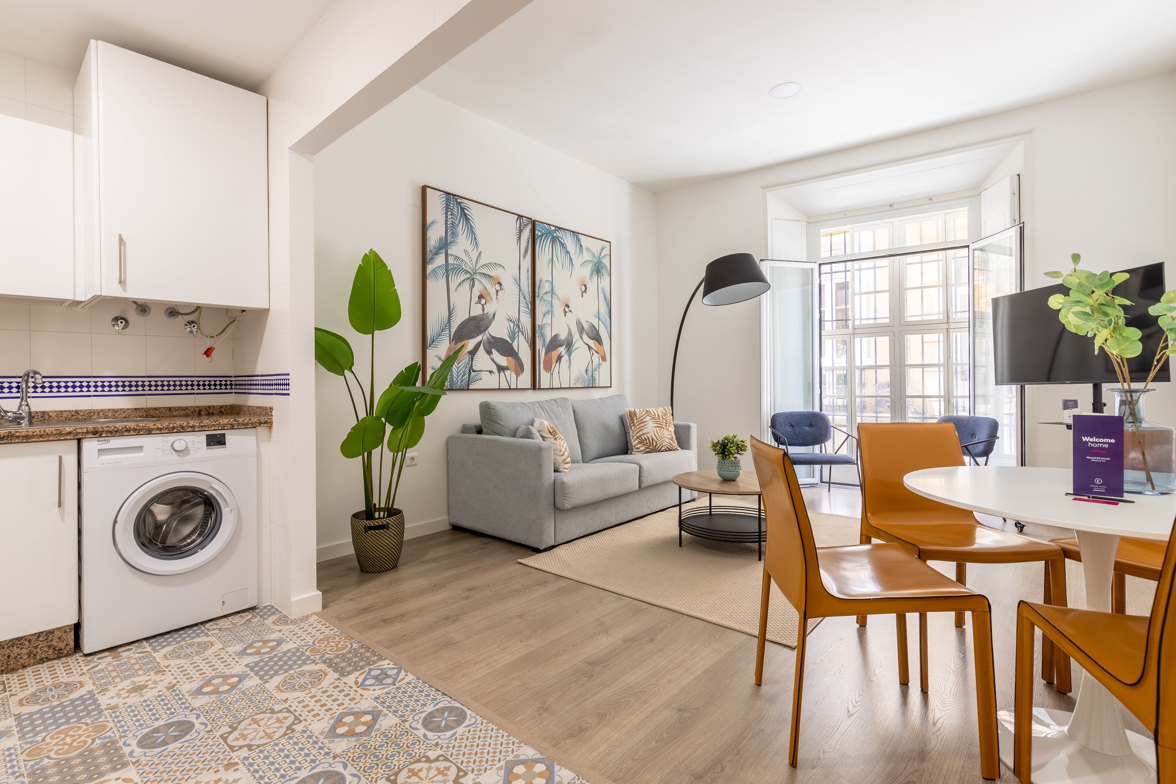 Un appartement moderne comprenant une cuisine, un espace de vie et un coin repas. Il est équipé d’un lave-linge, d’un canapé, d’une table basse et d’un téléviseur.