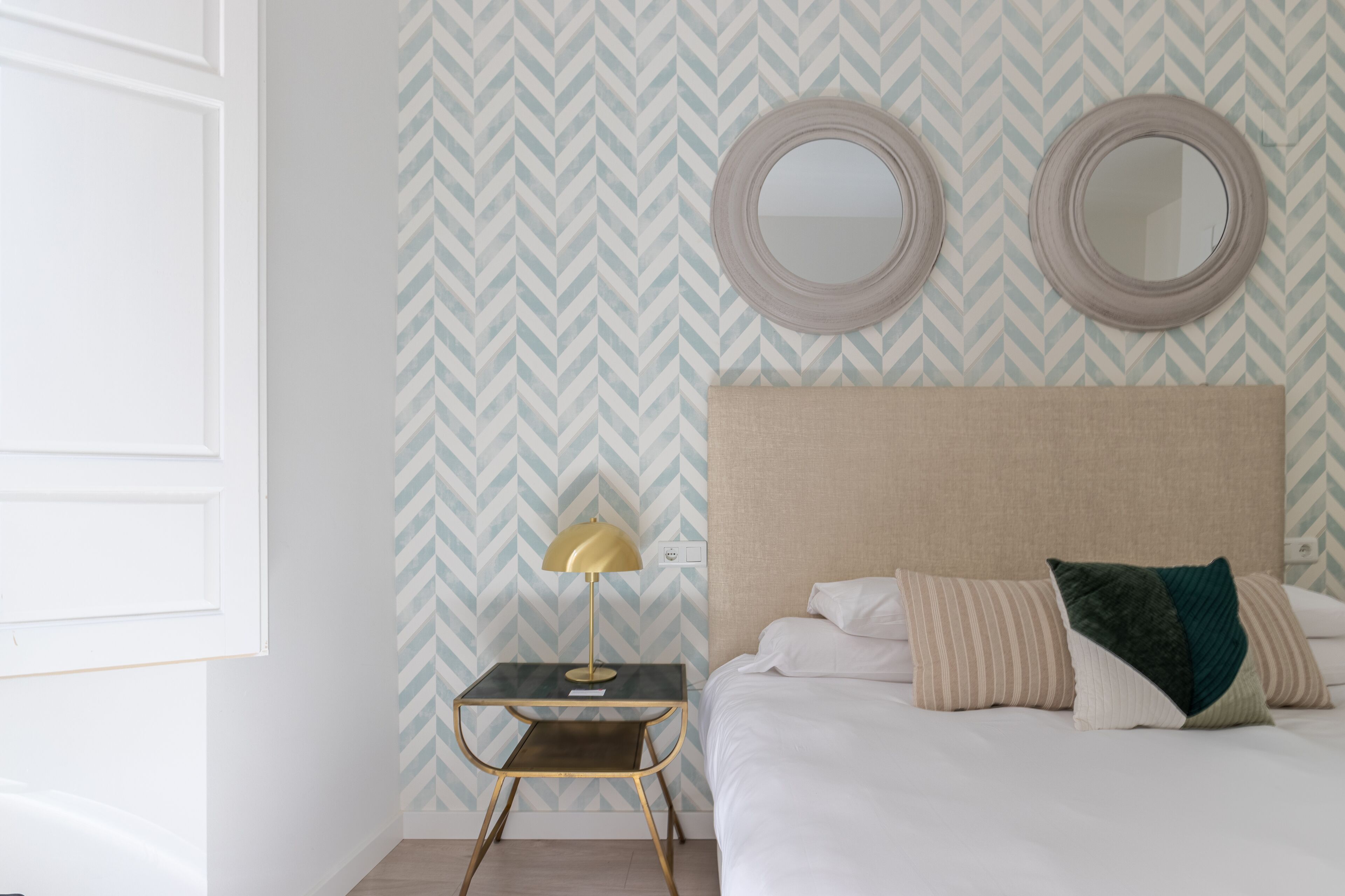 Un dormitorio ordenado con cama, mesitas de noche y dos espejos en la pared.