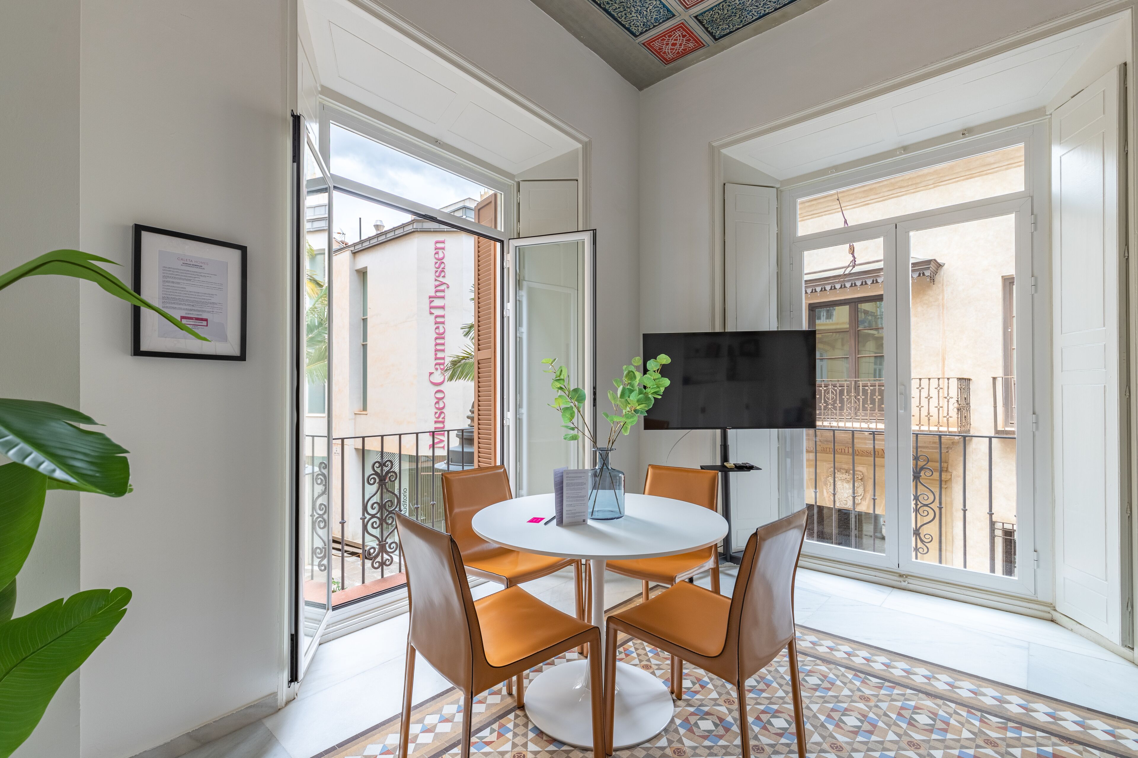 Un coin repas comprenant une table ronde, quatre chaises, un vase avec des plantes et un téléviseur à écran plat.