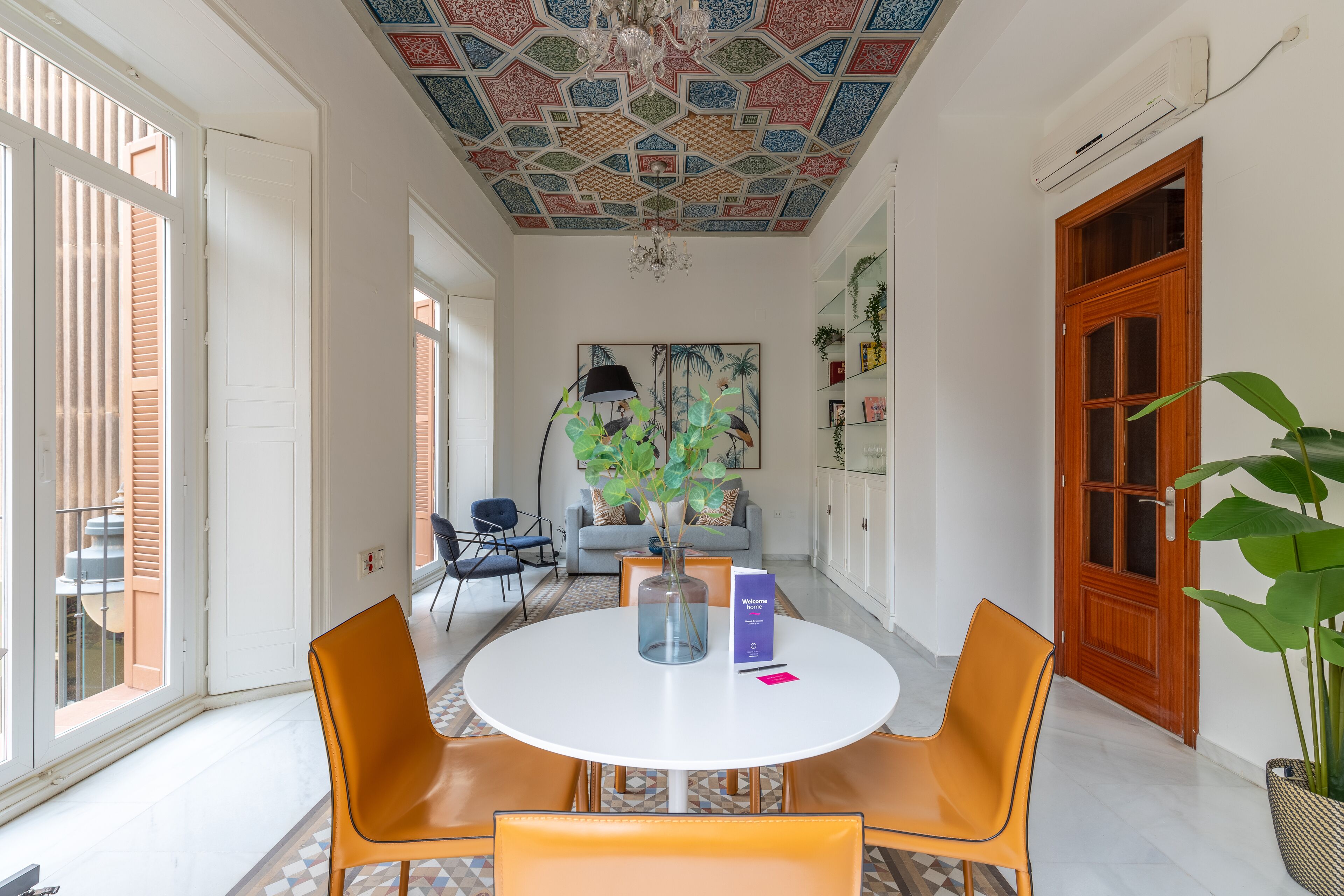 A modern dining area with a round table, orange chairs, and a decorative ceiling.