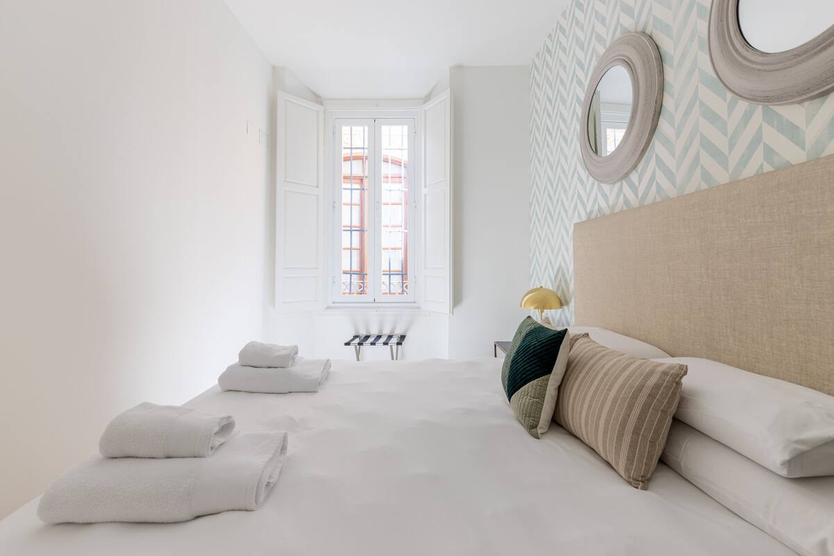 Ein Schlafzimmer mit einem Bett, Kissen, einer Bank und einem Fenster mit Blick.