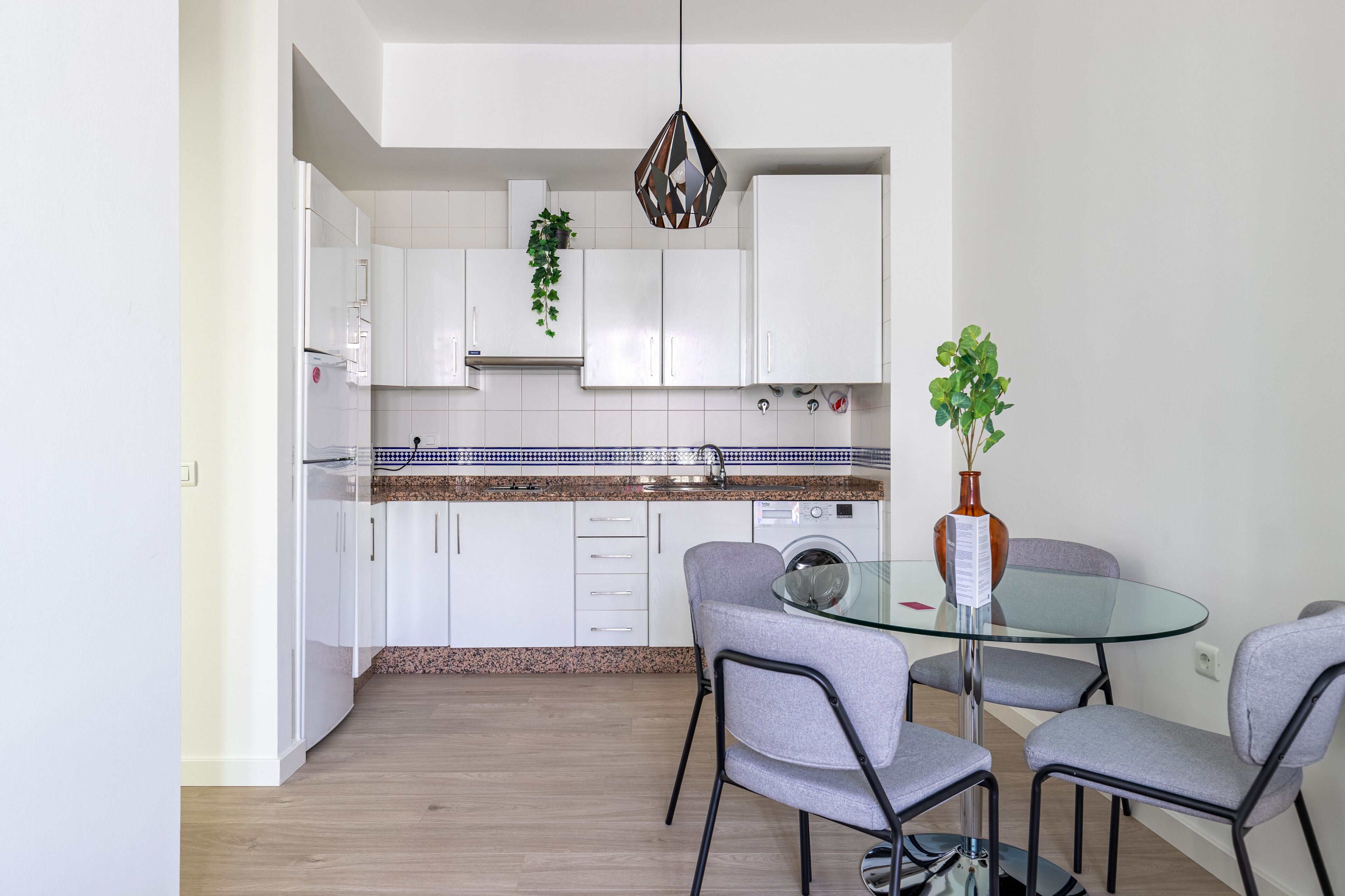 A modern kitchen with white cabinets, a granite countertop, and a glass dining table with four chairs.