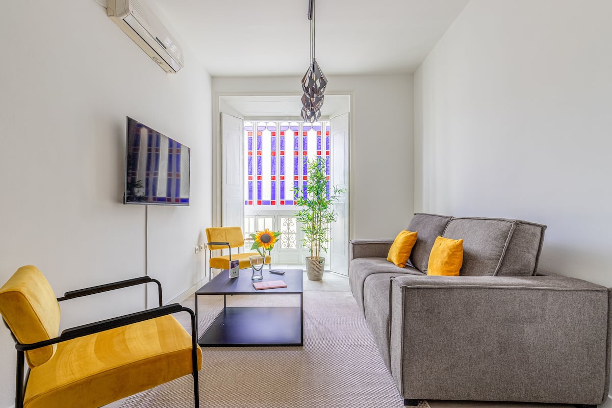 Ein modernes Wohnzimmer mit Sofa, Ohrensessel, Couchtisch und einem Blumentopf.