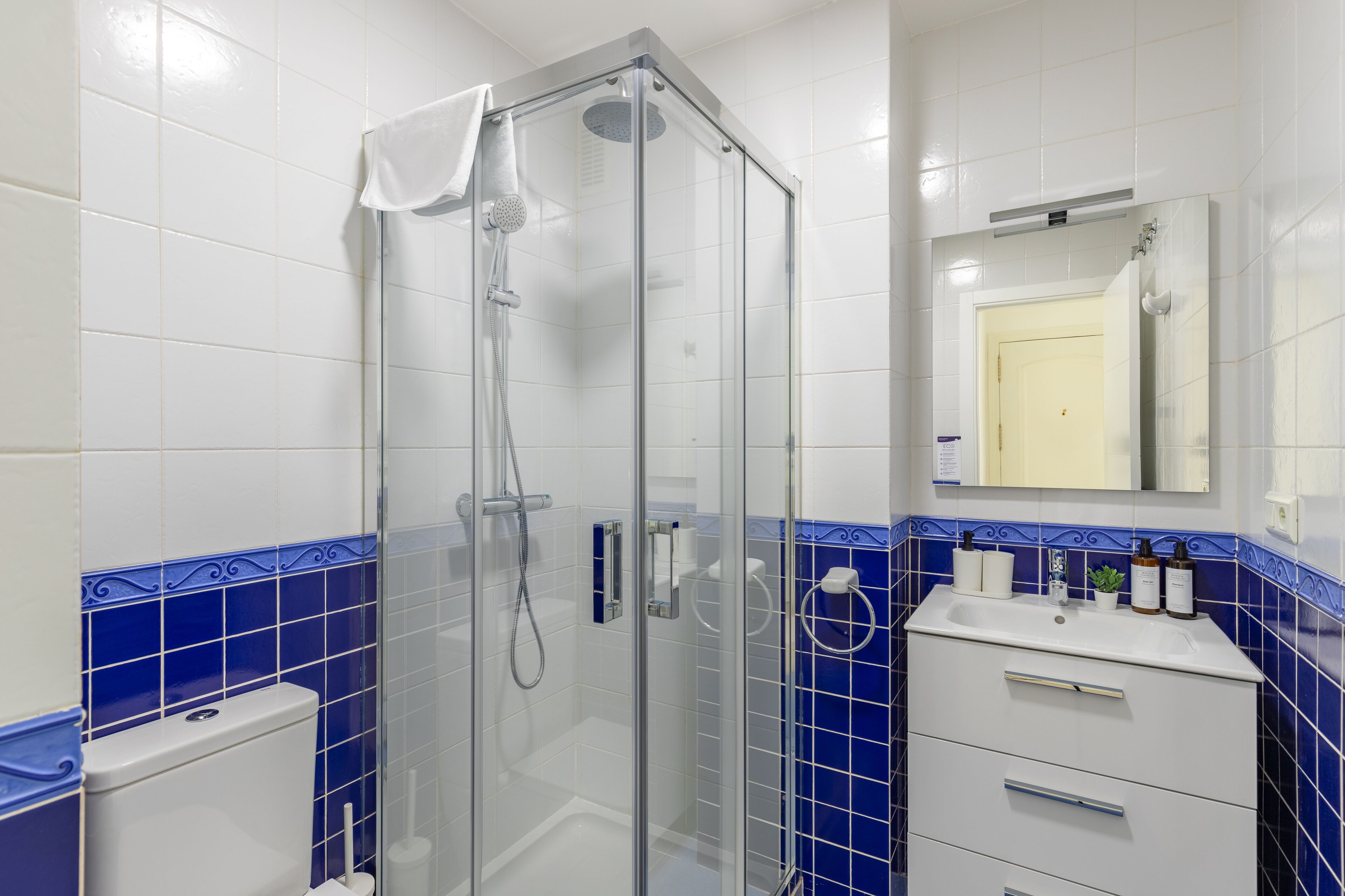 Ein Badezimmer mit einer Duschkabine, einem weißen Waschbecken mit Pflegeprodukten und blauen Fliesenwänden.