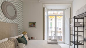 Une chambre d’hôtel comprenant un lit, une table de chevet, un miroir, un mur orné d’un motif en chevrons, une porte donnant sur un balcon et une étagère avec des serviettes.
