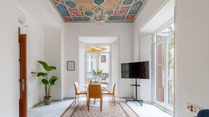 Un grand salon agrémenté d’un tapis à motifs, d’une table à manger avec des chaises, d’un téléviseur et d’une plante en pot.