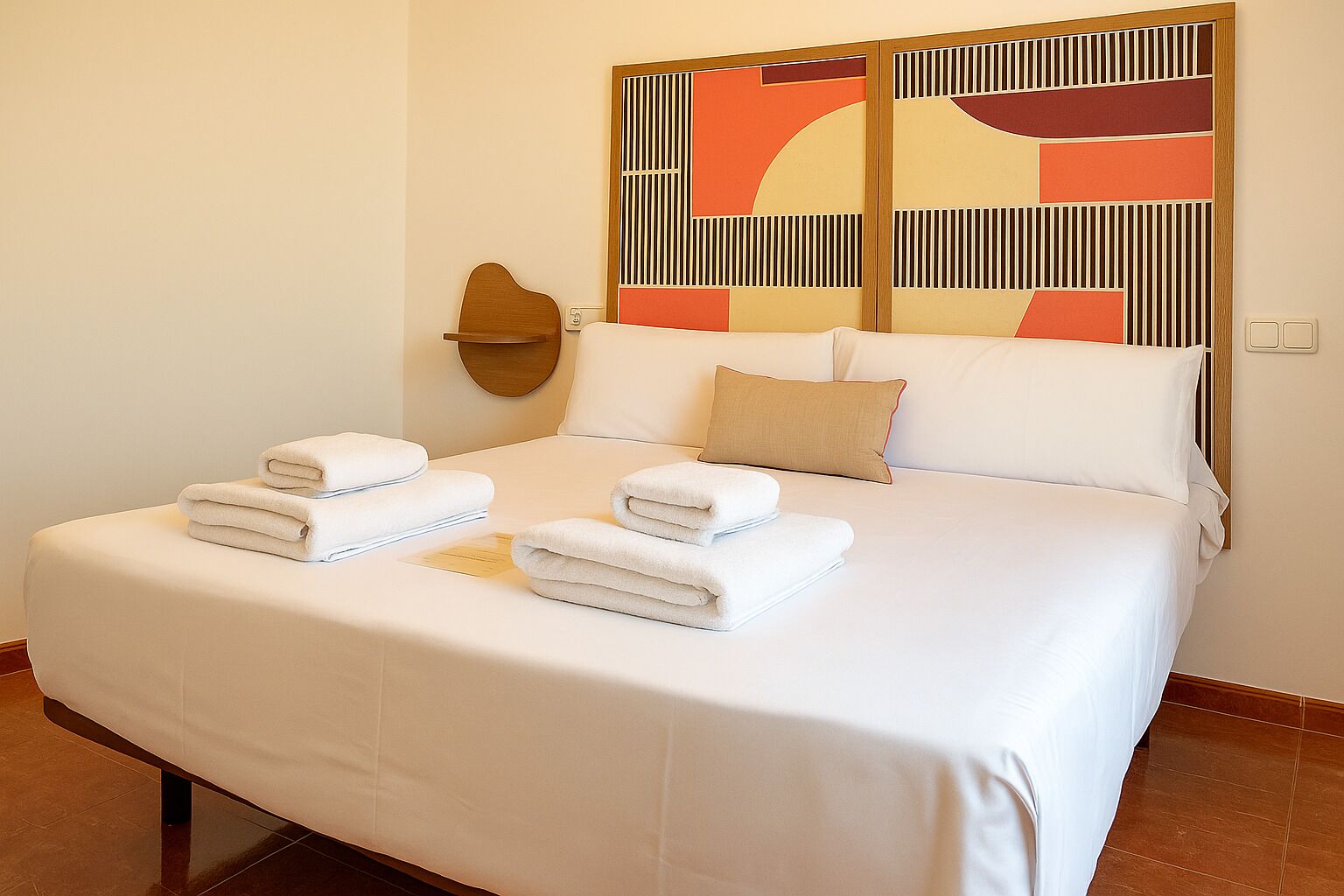 A hotel room with a large bed, a headboard with a geometric design, and a wall-mounted light fixture.