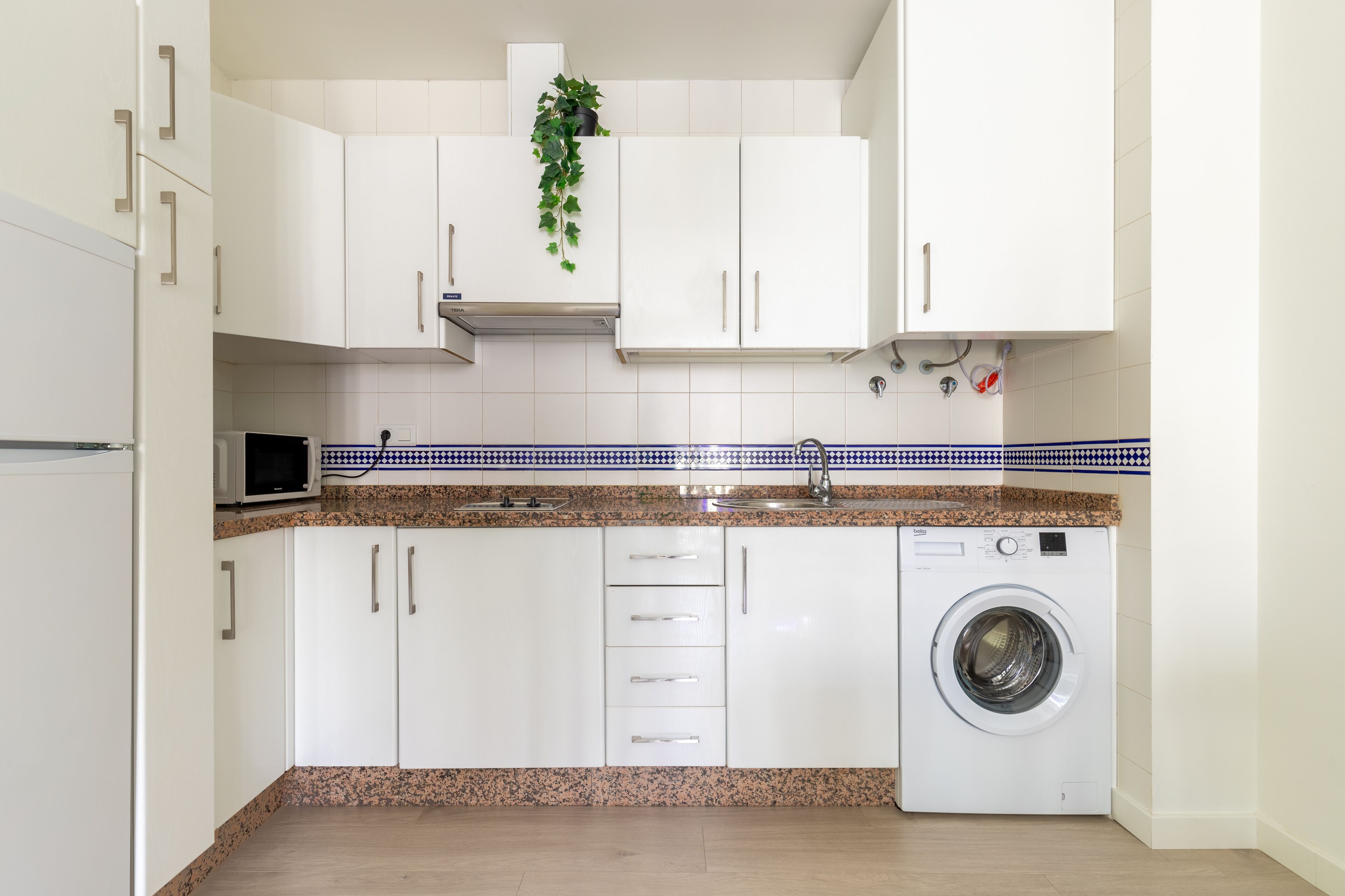 A compact kitchen with white cabinets, a built-in washing machine, and a microwave.