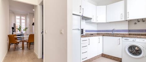 Una cocina moderna con armarios blancos, horno empotrado y lavadora.