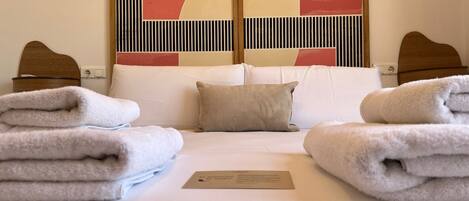A hotel room with a bed, pillows, a folded towel, and a sign on the bed.