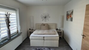 A bedroom with a bed, bedside tables, a decorative wall piece, a round rug, and a window with blinds. - Lounge 2 - Top apartment approx. 72sqm, air conditioning, parking at the house, all in (Koblenz)
