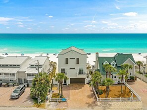 A beachfront property with a paved driveway, a white building with a green roof, and a clear view of the ocean.