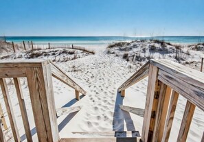 A wooden boardwalk leading to a beach with clear blue water and sandy dunes.