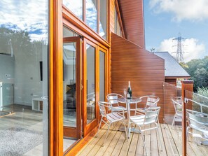 A wooden deck with a glass door leading to a room, a table with chairs, and a bottle of champagne. - Waterside Lodge Six - UK38264 (Elland)