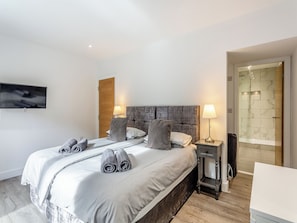 Una habitación de hotel moderna con una cama grande, un televisor montado en la pared y un área de ducha con puerta de vidrio.