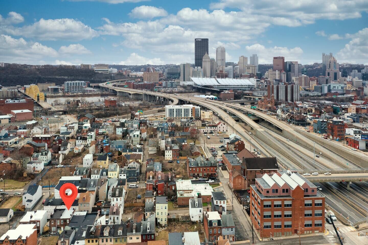 Une vue urbaine avec un pont imposant, un mélange de bâtiments résidentiels et commerciaux, et un grand stade en arrière-plan.