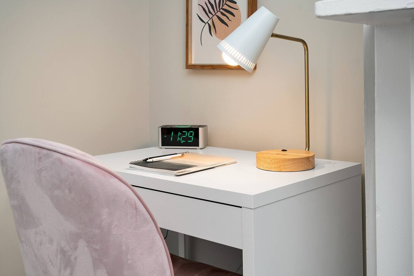 A white desk with a digital clock, a notebook, a pen, and a lamp.