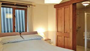 A bedroom with a bed, a wooden wardrobe, a shower area, and a window with curtains.
