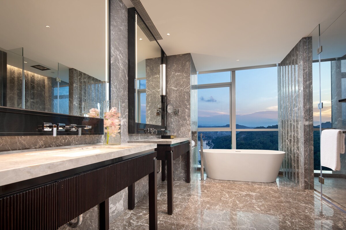 A modern bathroom with a large bathtub, a vanity with a mirror, and a view of the mountains through large windows.
