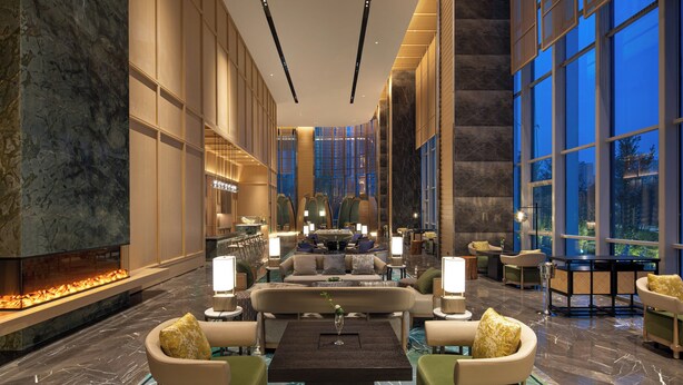 A spacious lobby with a central seating area, a fireplace, and large windows offering a view of the cityscape. - HUALUXE Yibin by IHG (Yibin)