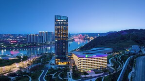 A modern hotel with a prominent tower and a curved building, surrounded by a landscaped area and a river. - HUALUXE Yibin by IHG (Yibin)