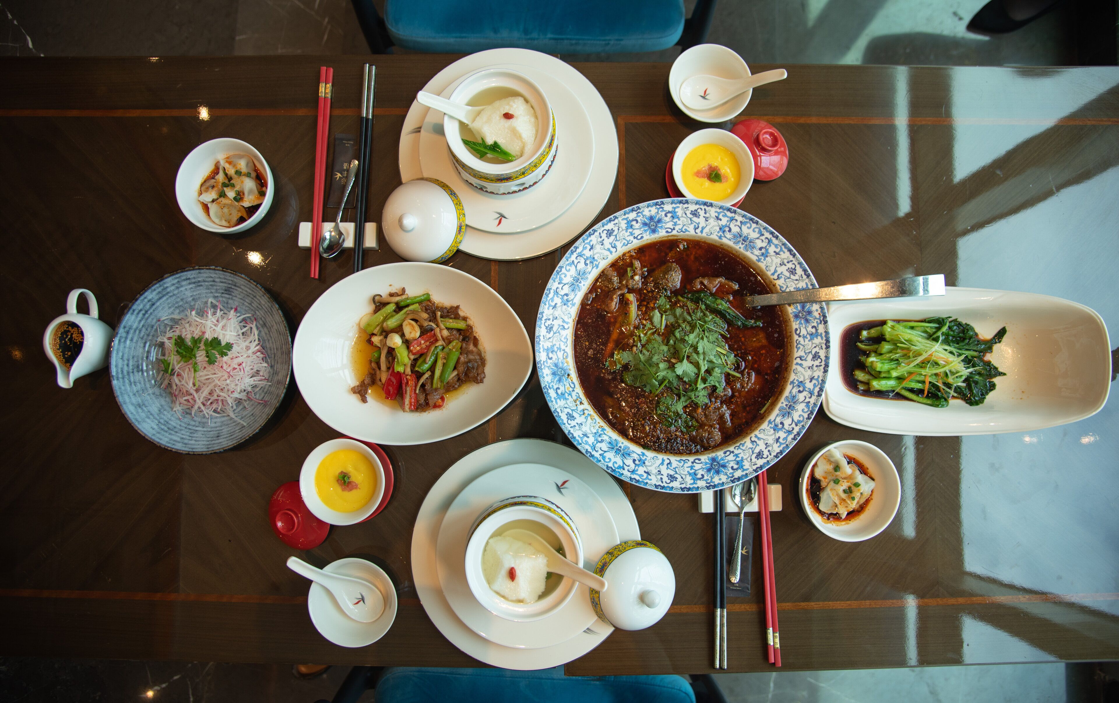 A dining table with various dishes, including soup, vegetables, and meat, arranged for a meal.