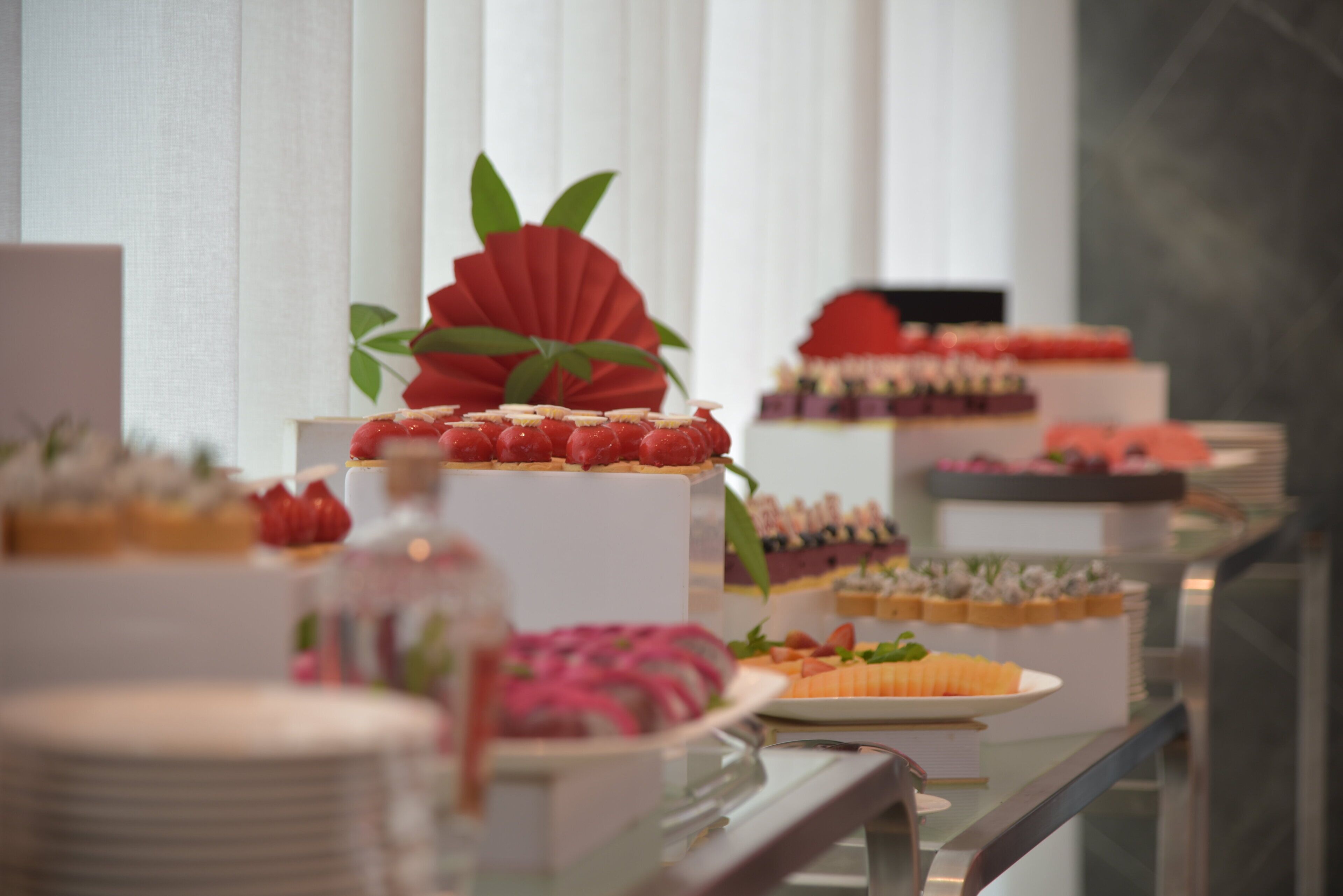A buffet with various desserts and a decorative red fan on a white pedestal.