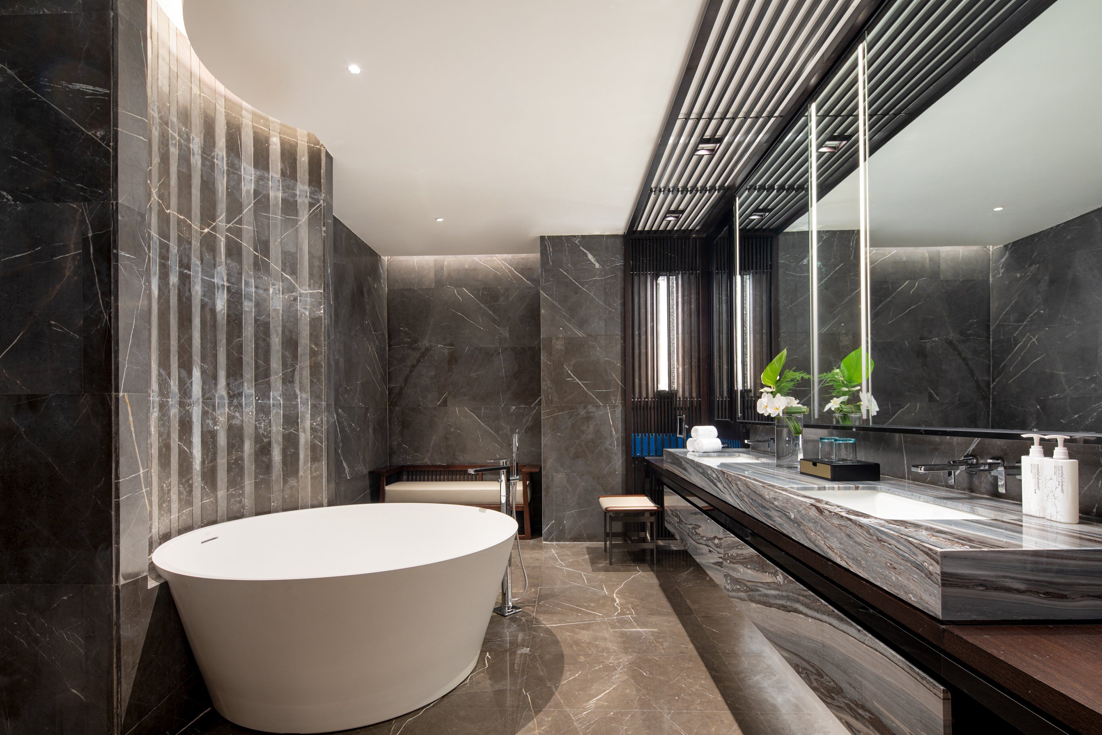A modern bathroom with a large bathtub, a vanity with a mirror, and marble walls.