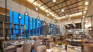 A modern dining area with multiple tables and chairs, large windows, and hanging spherical light fixtures. - HUALUXE Yibin by IHG (Yibin)
