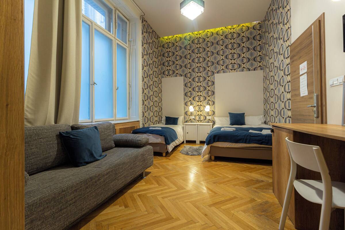 A bedroom with a wooden floor, two beds, a sofa, a desk, and a chair.