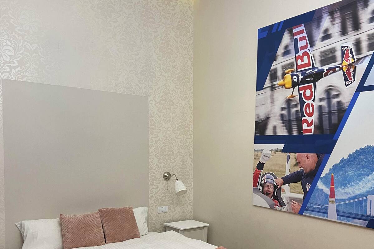A bedroom with a bed, bedside table, lamp, and a wall with a Red Bull advertisement.